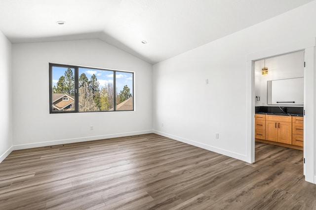 unfurnished bedroom with baseboards, wood finished floors, ensuite bath, and lofted ceiling