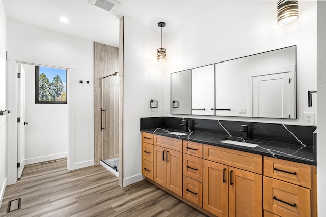 bathroom featuring wood finished floors, a shower stall, double vanity, a sink, and visible vents