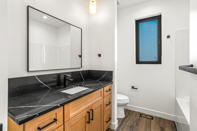 full bath with wood finished floors, a washtub, toilet, vanity, and baseboards