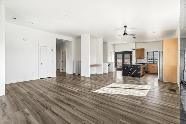 unfurnished living room with dark wood-style flooring, ceiling fan, visible vents, and baseboards