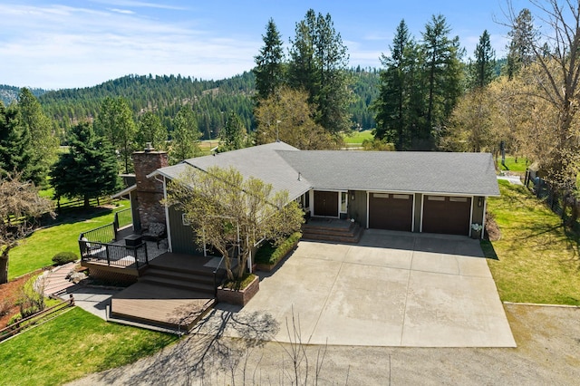 view of front of house featuring concrete driveway, a front lawn, a view of trees, and a garage