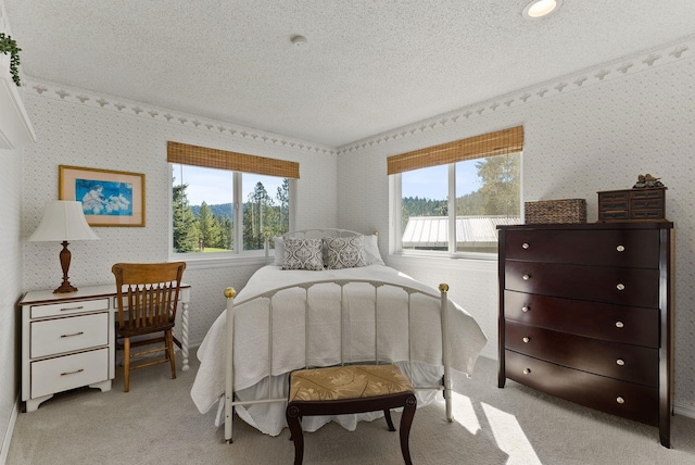 bedroom with wallpapered walls, a textured ceiling, and light carpet