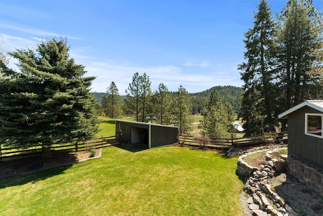 view of yard with a view of trees, an outbuilding, and fence