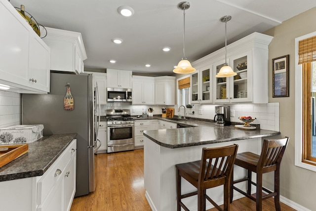 kitchen with backsplash, dark countertops, a sink, a peninsula, and appliances with stainless steel finishes