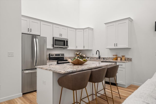kitchen featuring light wood-style floors, appliances with stainless steel finishes, light stone counters, a kitchen island, and a breakfast bar area