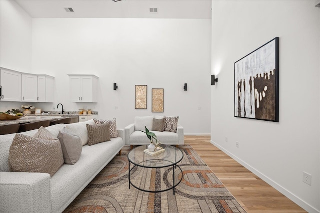 living room with visible vents, baseboards, a towering ceiling, and light wood-style floors