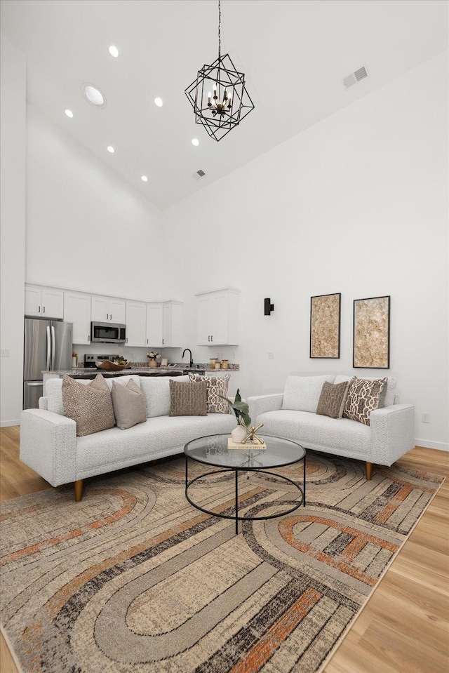 living area with recessed lighting, a towering ceiling, an inviting chandelier, visible vents, and light wood-type flooring