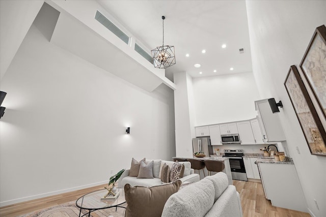 living room with light wood-type flooring, a towering ceiling, baseboards, and an inviting chandelier
