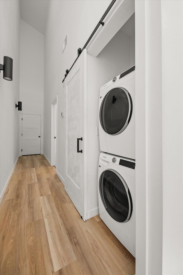 laundry room featuring a barn door, laundry area, light wood-style floors, baseboards, and stacked washer and dryer