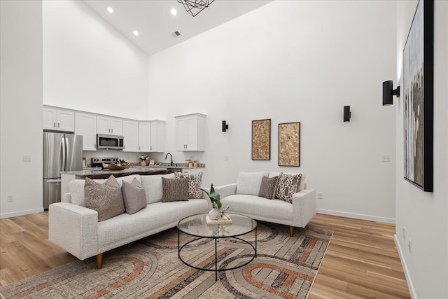 living area with baseboards, light wood-style flooring, and high vaulted ceiling
