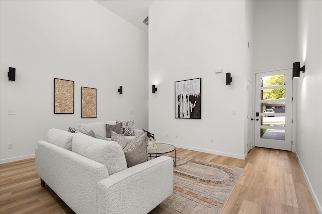 living room with baseboards, a towering ceiling, and light wood-style flooring