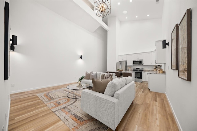 living area featuring baseboards, a high ceiling, light wood-style floors, and an inviting chandelier