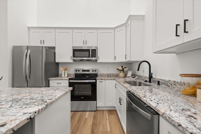 kitchen with white cabinetry, stainless steel appliances, light wood finished floors, and a sink