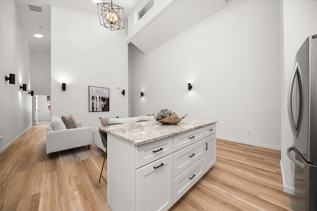 kitchen with visible vents, a towering ceiling, light wood-style flooring, and freestanding refrigerator