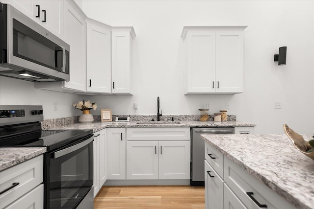 kitchen featuring a sink, light wood-type flooring, white cabinetry, appliances with stainless steel finishes, and light stone countertops