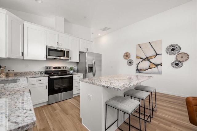 kitchen with light wood-style flooring, stainless steel appliances, visible vents, and a breakfast bar area