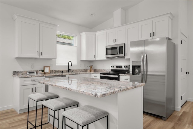 kitchen with light stone counters, light wood finished floors, white cabinets, lofted ceiling, and appliances with stainless steel finishes