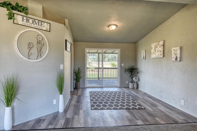 entrance foyer with vaulted ceiling, a textured wall, wood finished floors, and baseboards