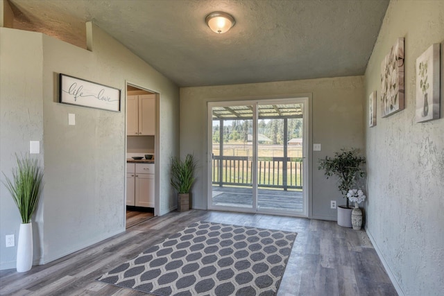 doorway to outside featuring wood finished floors, a textured ceiling, and a textured wall