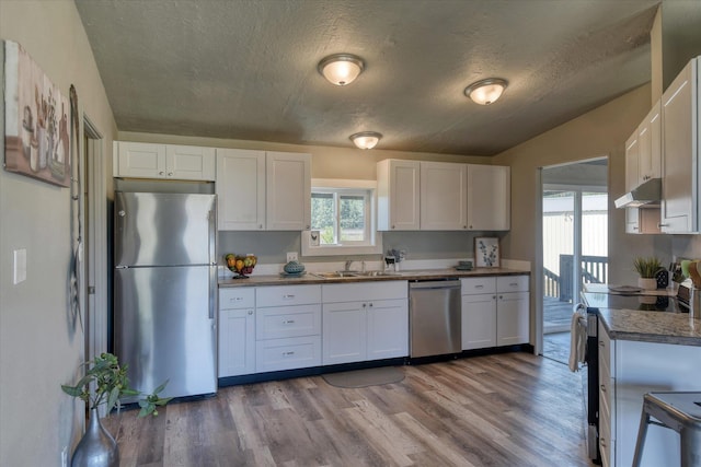 kitchen featuring white cabinets, a wealth of natural light, a sink, under cabinet range hood, and appliances with stainless steel finishes
