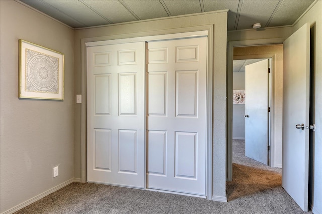 unfurnished bedroom featuring baseboards, carpet flooring, a closet, and crown molding