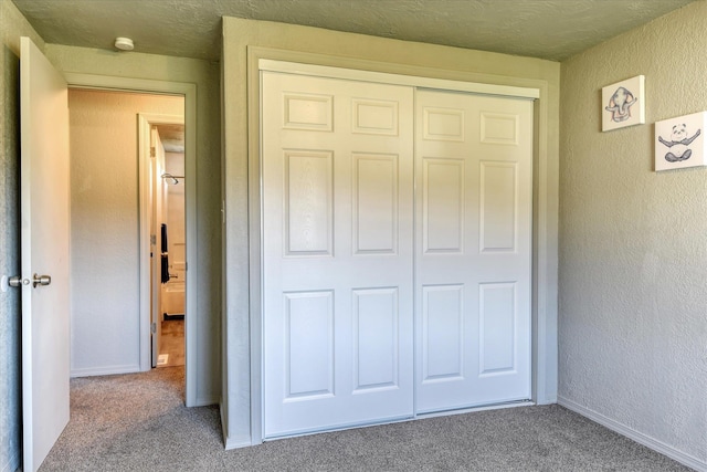 unfurnished bedroom featuring a textured wall, a closet, carpet flooring, and baseboards