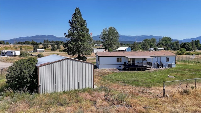 back of property featuring an outdoor structure, a deck with mountain view, a lawn, and fence