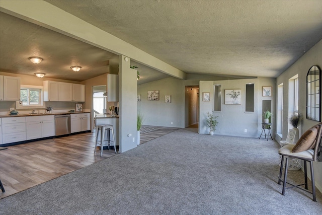 unfurnished living room featuring carpet flooring, a sink, a textured ceiling, baseboards, and lofted ceiling