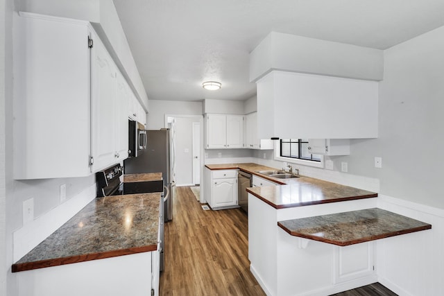 kitchen with dark countertops, wood finished floors, a peninsula, appliances with stainless steel finishes, and white cabinetry