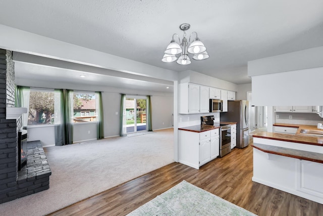 kitchen with stainless steel appliances, wood finished floors, a sink, a fireplace, and white cabinetry