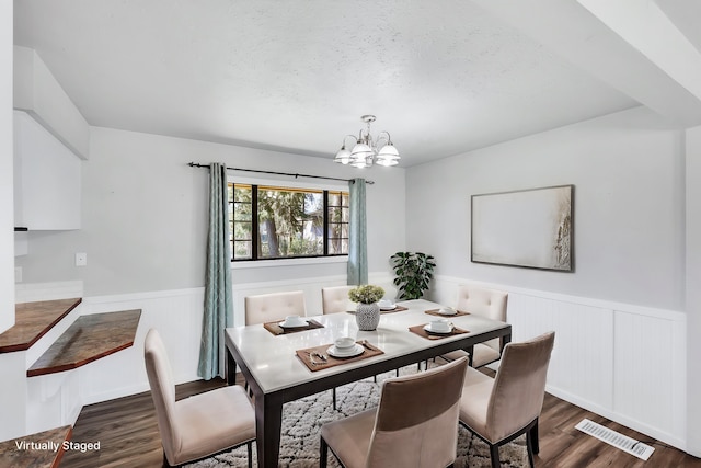 dining room with a textured ceiling, dark wood-style flooring, wainscoting, visible vents, and a chandelier