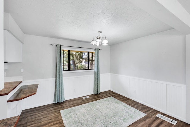 unfurnished dining area with wainscoting, a chandelier, visible vents, and a textured ceiling