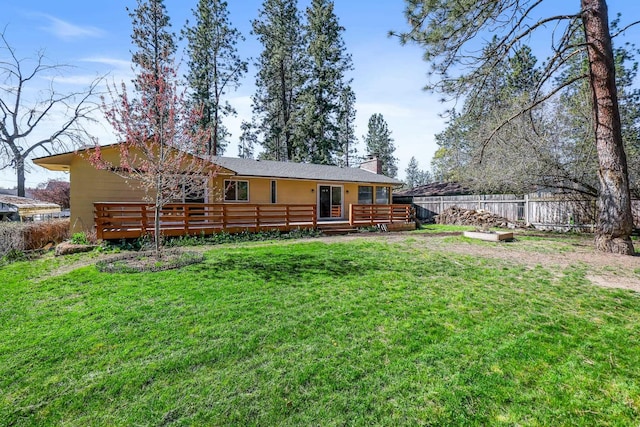 back of house featuring a wooden deck, a lawn, a chimney, and fence