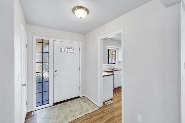 entrance foyer featuring light wood finished floors, baseboards, visible vents, and a textured ceiling