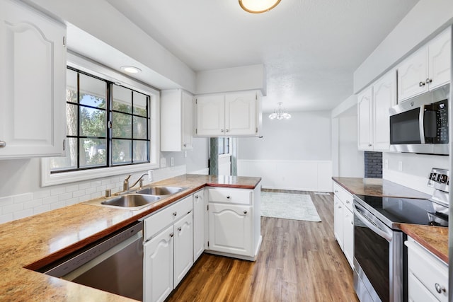 kitchen featuring a peninsula, appliances with stainless steel finishes, a sink, and white cabinetry