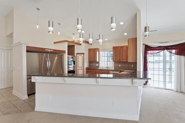 kitchen featuring dark stone countertops, a sink, brown cabinets, stainless steel appliances, and light colored carpet