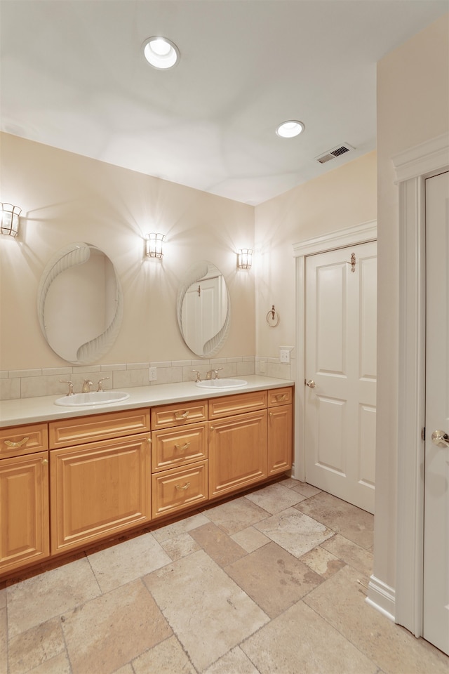 bathroom with stone tile floors, a sink, visible vents, and double vanity