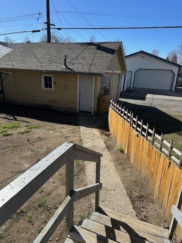 exterior space featuring an outdoor structure, fence, roof with shingles, and a garage