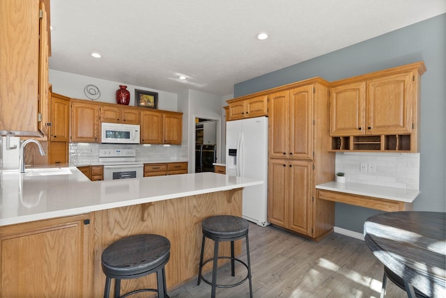 kitchen with a peninsula, a sink, light wood-type flooring, backsplash, and white appliances