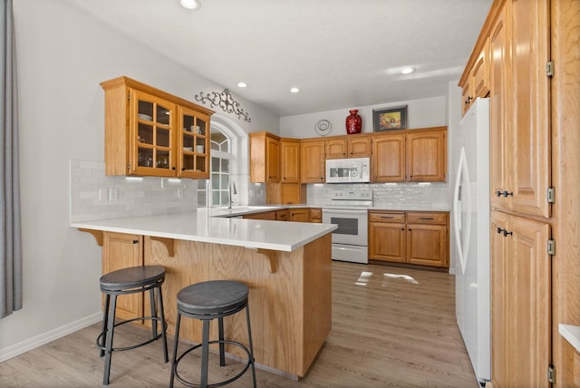 kitchen featuring white appliances, glass insert cabinets, a breakfast bar area, backsplash, and a peninsula