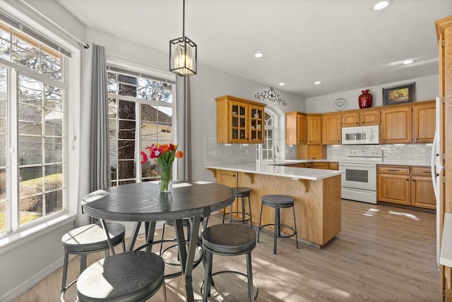 kitchen featuring a peninsula, tasteful backsplash, a healthy amount of sunlight, and white appliances