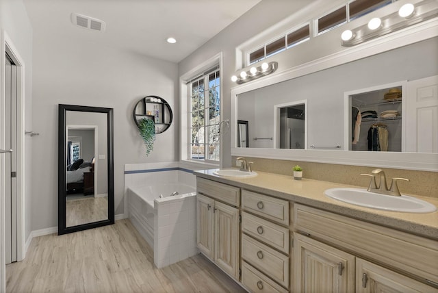 full bathroom with wood finished floors, visible vents, a garden tub, and a sink