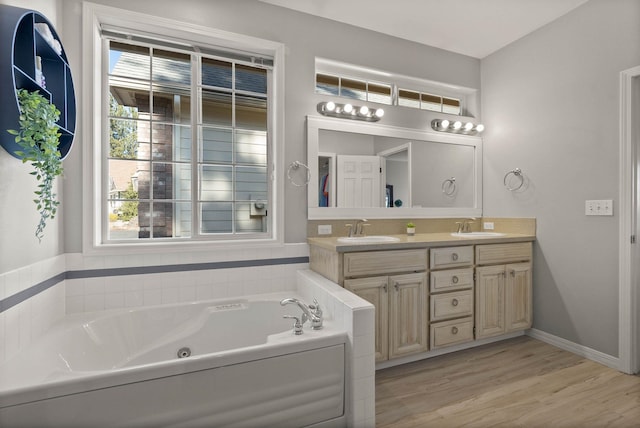 full bath featuring double vanity, a tub with jets, wood finished floors, and a sink