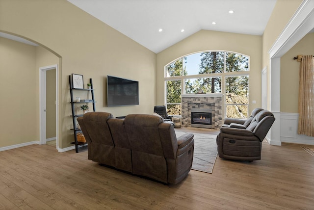 living area with arched walkways, recessed lighting, wood finished floors, a stone fireplace, and high vaulted ceiling