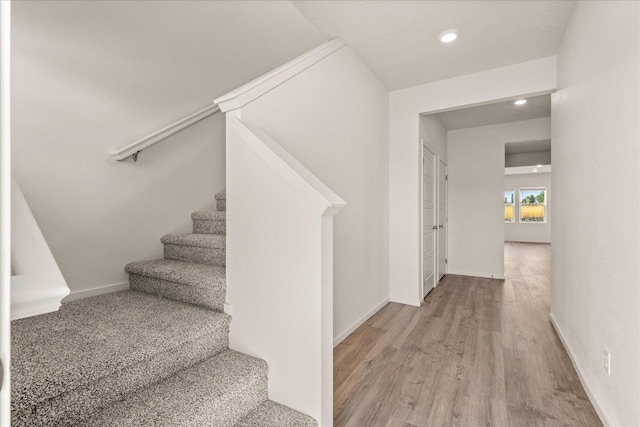 stairway with baseboards, wood finished floors, and recessed lighting