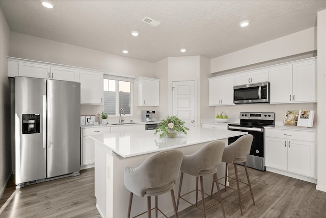 kitchen featuring a center island, a sink, light wood-type flooring, white cabinetry, and appliances with stainless steel finishes