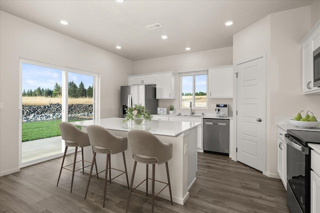 kitchen with a sink, appliances with stainless steel finishes, dark wood-type flooring, visible vents, and a kitchen island