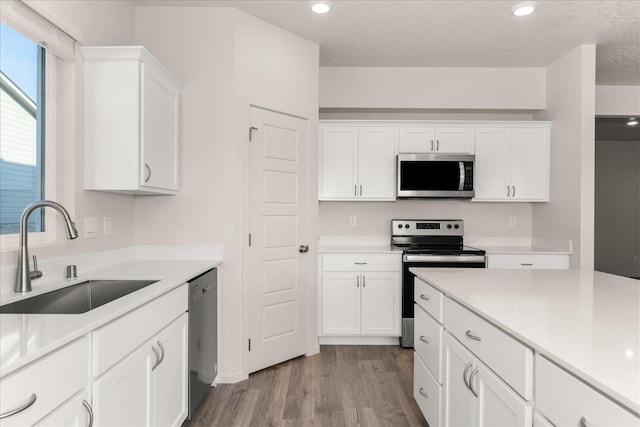 kitchen with white cabinets, a sink, dark wood-style flooring, light countertops, and appliances with stainless steel finishes