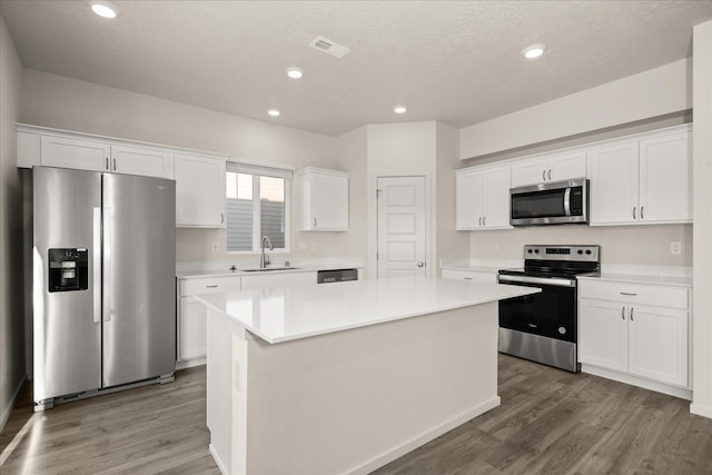kitchen with a sink, white cabinetry, light countertops, appliances with stainless steel finishes, and a kitchen island