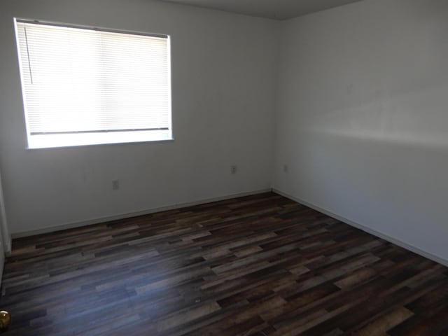 spare room with baseboards and dark wood-style flooring